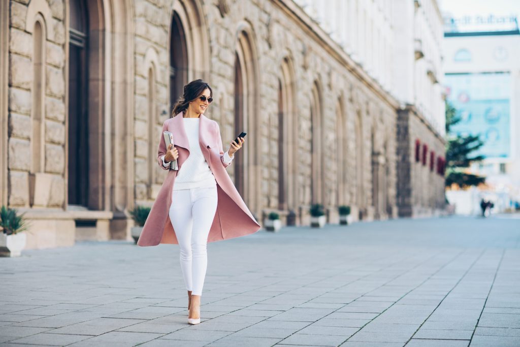 Elegant young woman walking on the square and texting in urban environment. Social currency and branding concepts